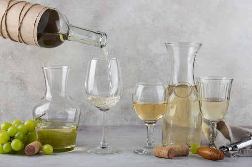 Pouring different types of white wine in different glasses and jars with some white grape and wine bottle opener on the table.-Bottle Barn