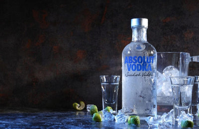 A bottle of Absolute vodka with some vodka shot glass and ice on the floor-Bottle Barn